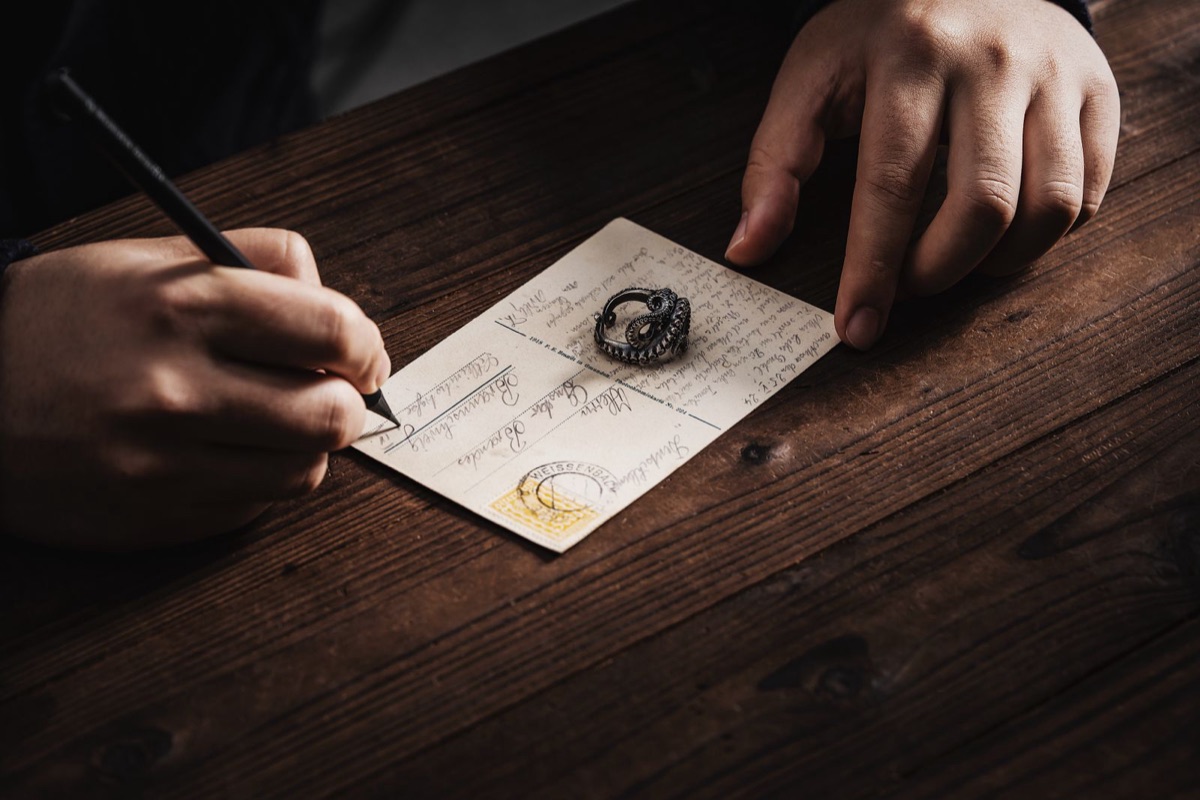 Hands writing a postcard at a wooden desk